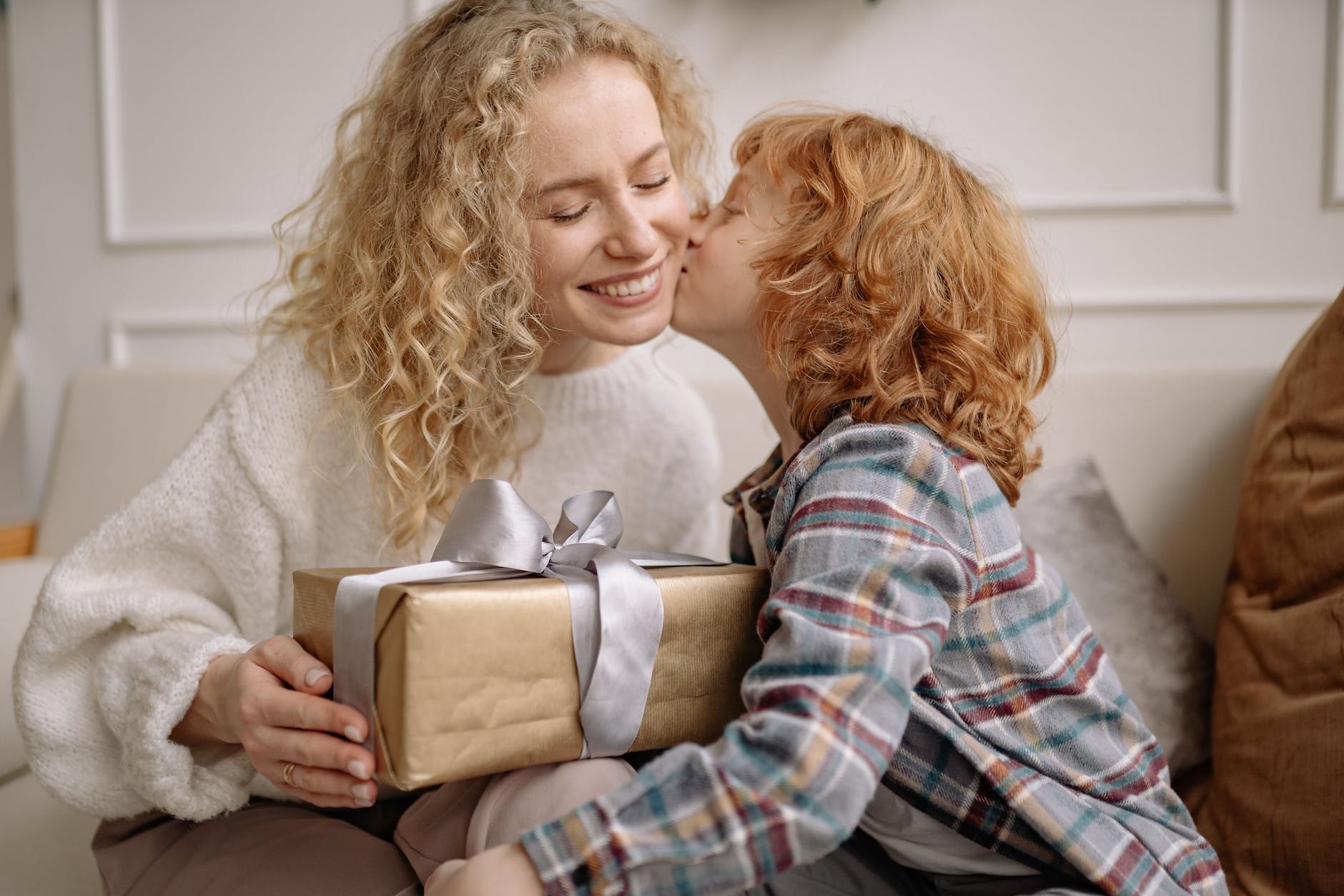 a boy in plaid shirt kissing a woman in white top holding a gift box