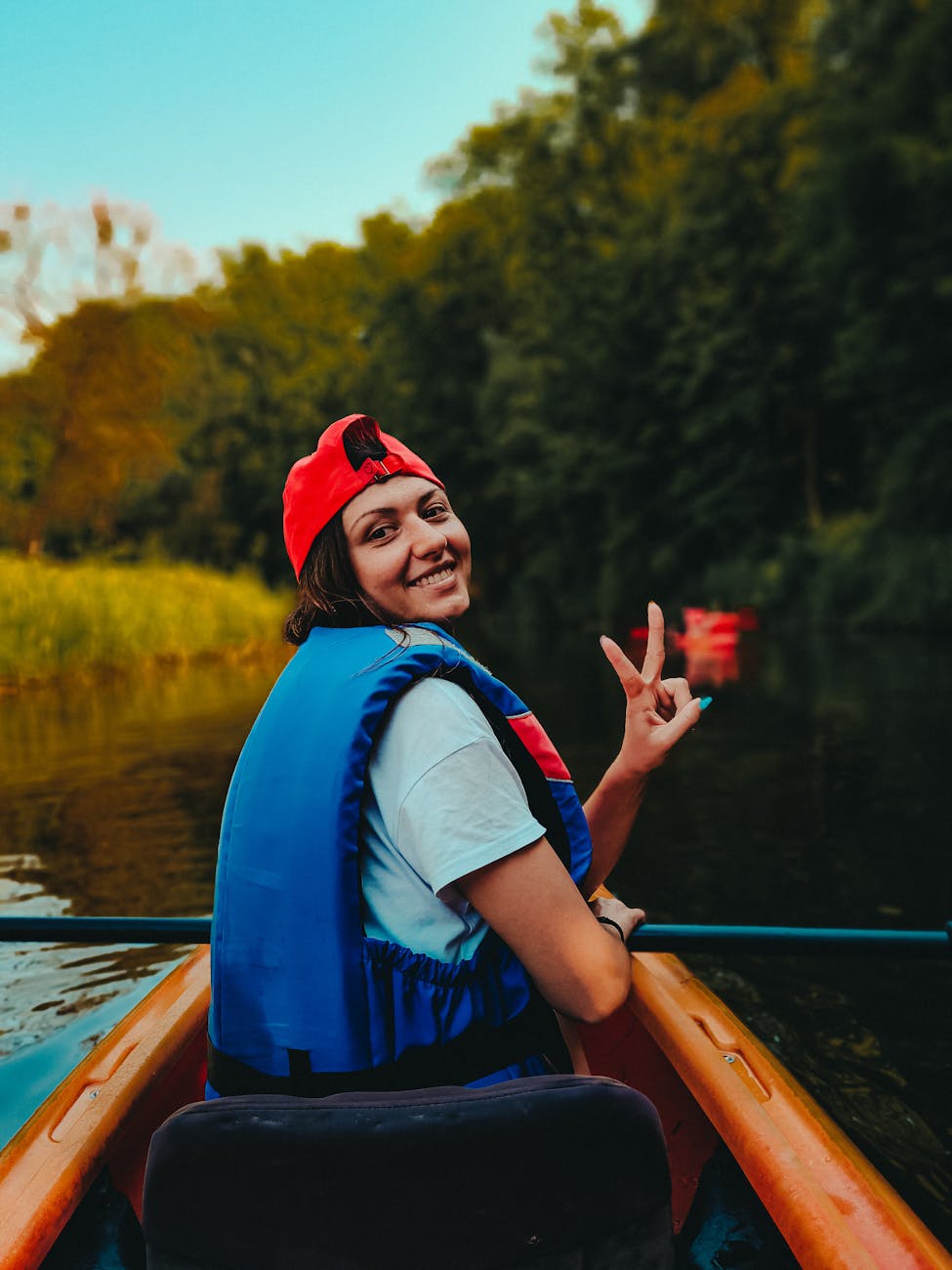 woman in blue and red jacket wearing red cap riding on orange kayak